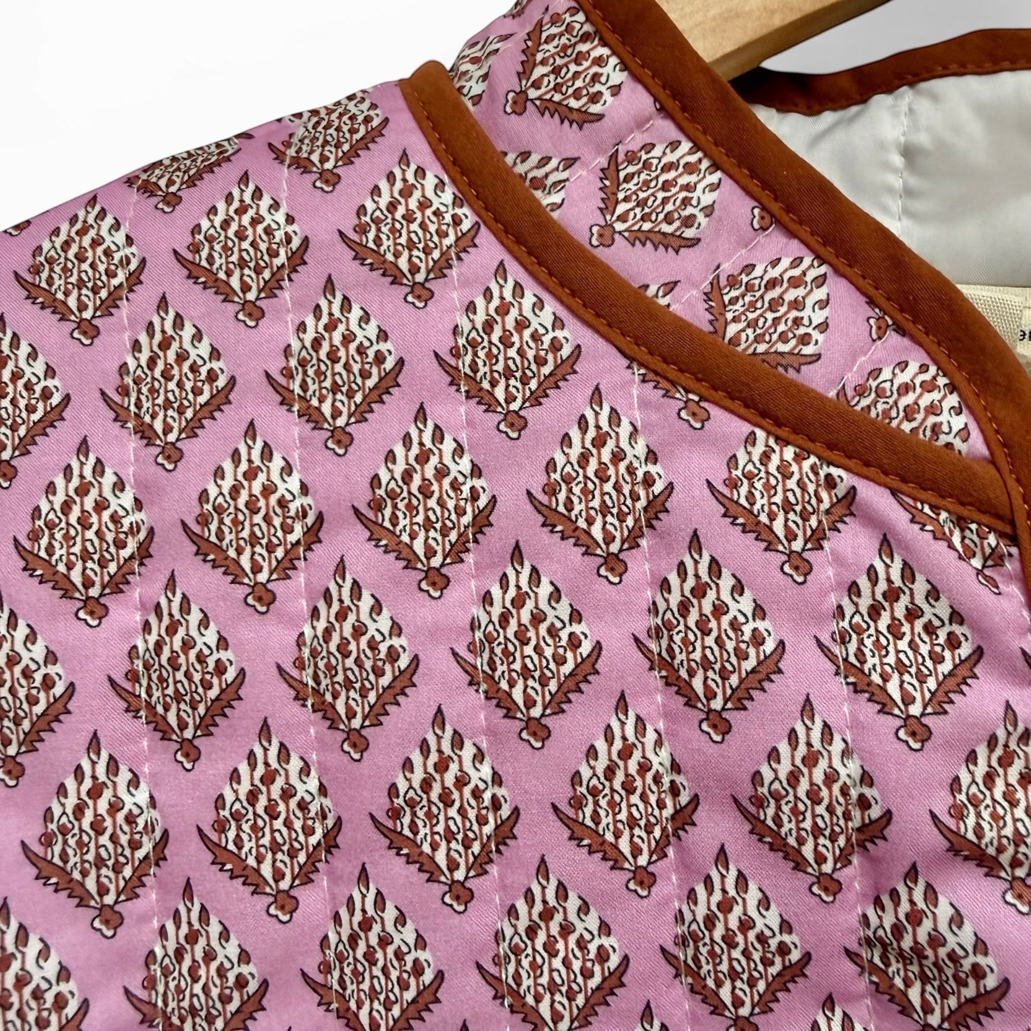The Marley Edit pink quilted jacket with block print pattern and tan binding. Lightweight, relaxed fit with button front and patch pockets.