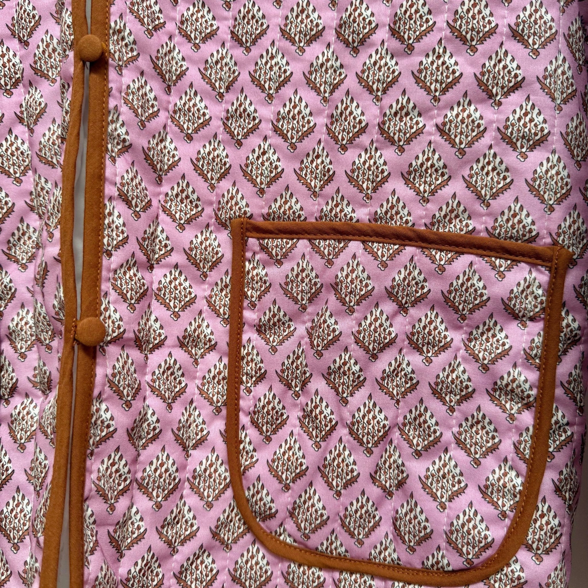 The Marley Edit pink quilted jacket with block print, tan binding, and button front. Lightweight and fully lined.